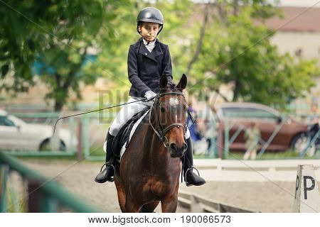 Young teenage girl in helmet riding horse on dressage equestrian competition