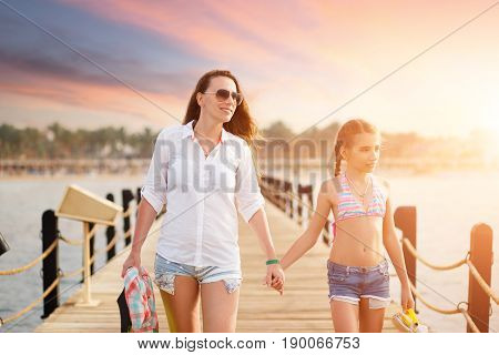 Young woman with her daughter strolling along pier on sea vacation