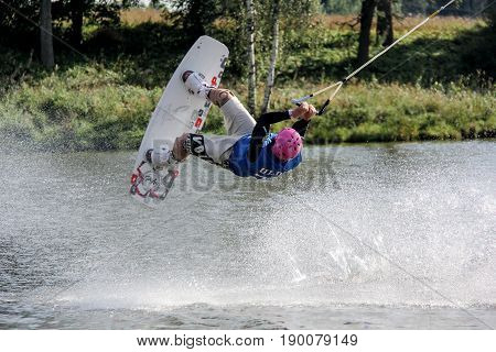 Man is among a splash of water he is riding a wakeboard  and jumping upside down