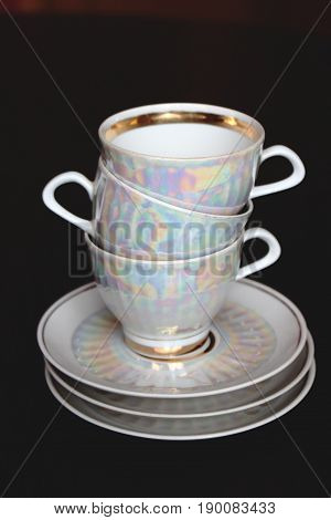 A pile of white iridescent tea cups and saucers