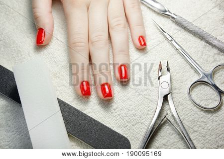 nail scissors file and clippers to remove the cuticle care products on white towel with woman manicured red nails