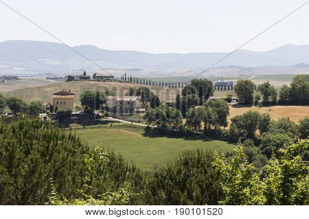VAL D'ORCIA. ITALY - JUNE 3 2017: Hills surrounding Val D'orcia area in Tuscany region of Italy with houses and cypress in the background