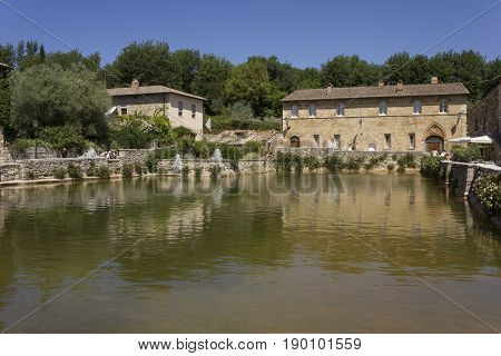BAGNO VIGNONI, ITALY - JUNE 3 2017: Piazza delle sorgenti medieval square in Bagno Vignoni with a lake of hot spring water and people looking at it
