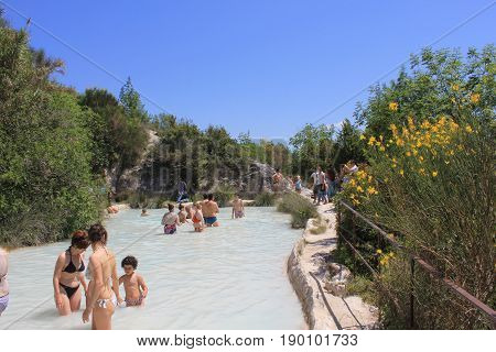 BAGNO VIGNONI, ITALY - JUNE 3 2017: People bathing in the free area of Bagno Vignoni in Tuscany Italy free accessible hot springs puddle trough vegetation