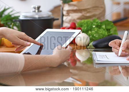 Human hands of two female persons using touchpad for making menu in the kitchen. Closeup of two women are making online shopping by tablet computer and credit card. Cooking and shopping concept