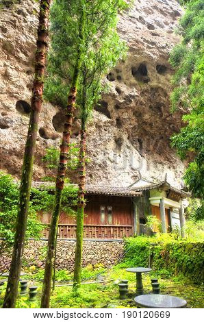 A chinese building below burial caves in the rocky cliff in the Fangdong Scenic Area on Yandangshan mountains located in Zhejiang province China. the chinese characters mean forest tea garden on the building.