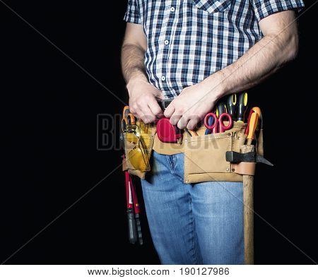 detail of handyman with leather toolsbelt and tools on dark background