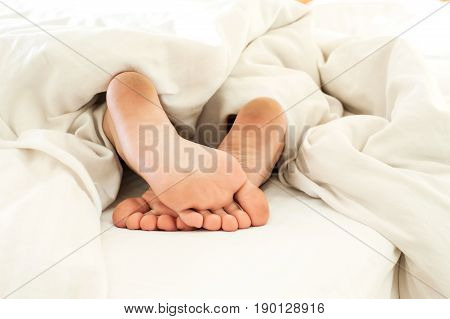 Sleeping child dirty feet on white bed linen from backside. Horizontal indoors close-up image.