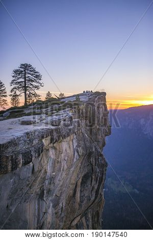 A small group of people sit at Taft Point in Yosemite at sunset.