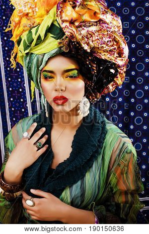 beauty bright woman with creative bright make up, many shawls on head like cubian, ethno look closeup