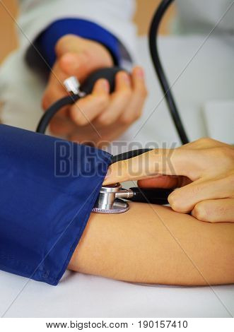 Close up of a young doctor using the stethoscope to hear the pulse while a woman is with a tensiometer in her arm, in a doctor consulting room background.