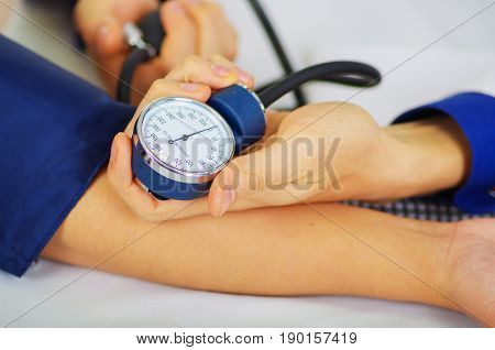 Close up of a young doctor using the stethoscope to hear the pulse while a woman is with a tensiometer in her arm, in a doctor consulting room background.