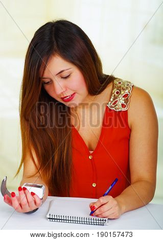 Beautiful young patient using an automatic tensiometer in her arm and taking notes of the results in his notebook, in a doctor consulting room background.