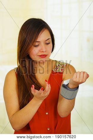 Beautiful young patient using an automatic tensiometer in her arm, in a doctor consulting room background.