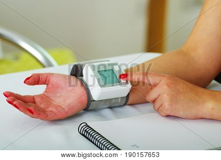 Close up of a young patient using an automatic tensiometer in her arm, in a doctor consulting room background.