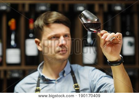 Bokal of red wine on background of male sommelier appreciating color, quality, flavor and sediments of drink. Professional degustation expert in winemaking.