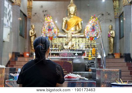 Rear view of Thai woman praying to Buddha in the temple
