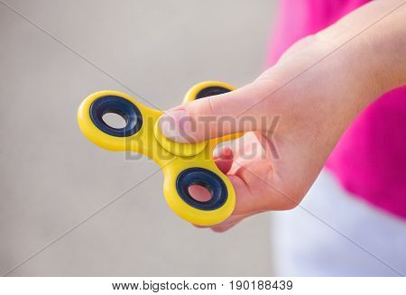 Little girl is playing a yellow spinner in her hand outdoors.