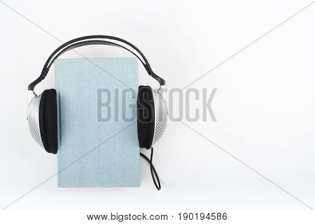Audiobook on white background. Headphones put over blue hardback book, empty cover, copy space for ad text. Distance education, e-learning concept