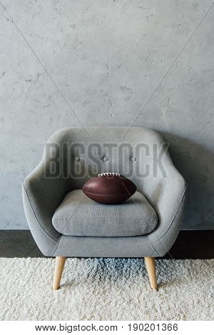 American Football Ball On Grey Textile Armchair At Empty Room