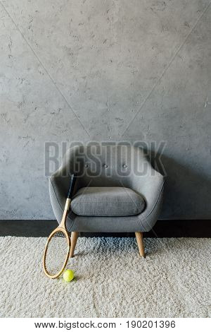 Tennis Racket And Ball With Grey Armchair At Empty Room