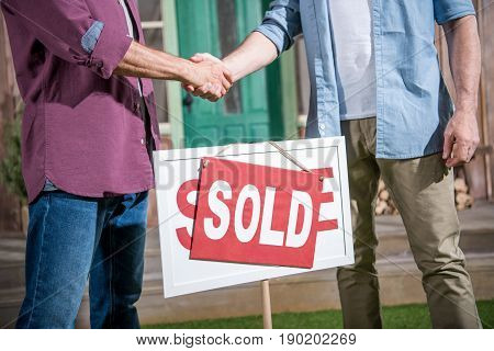 cropped view of men shaking hands with saleman and buying new house
