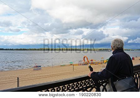Old man holding vintage umbrella looking far on the river beach outdoors sky background. Back side view of traveller explorer. Tourist senior