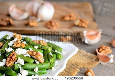 Healthy green beans salad with balsamic dressing. Warm green bean salad with cottage cheese, walnuts, garlic and spices on a plate and an old wooden table. Side dish or veggie main dish