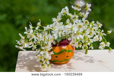 A bouquet of flowers birdcherry tree in orange wooden bowl on a wooden table on a dark green background, closeup