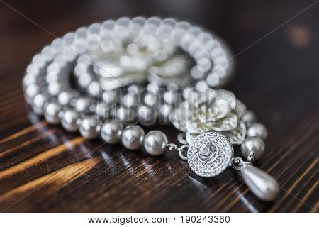 A necklace of black pearls with a large diamond surrounded by small stones and a silver brooch in the form of a flower lie on a dark brown wooden background.