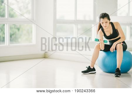 Sexy Asian girl exercising with dumbbell on fitness ball at fitness gym with copy space sport and healthy lifestyle concept