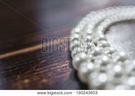 A pearl necklace of white pearls lies on a dark brown background on the right side of the frame.