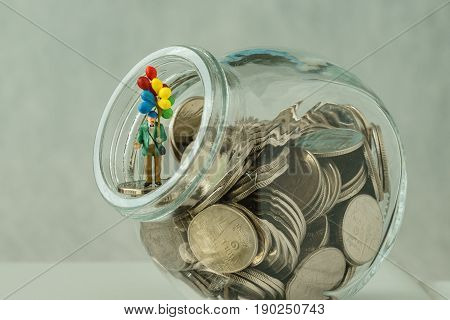Miniature figure old man with balloon standing on coins money in the jar as happy retirement financial or business concept.