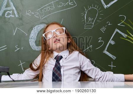 Girl schoolgirl knowledge, girl at the table wearing glasses at the blackboard.