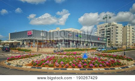 Nes Ziona, Israel-March 20, 2016:  Beautiful view of big flowerbed placed on traffic circle in front of supermarket Mega In The City and other commercial stores. Nice blue sky is over it. The complex is located at 1 Avner Ben Ner Street. Two white multi-s