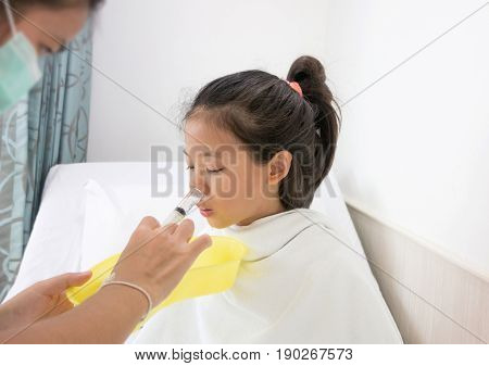 Ill young Asian girl with black hair sitting on bed in hospital. Sick kids cleaning nose with Nasal irrigation.