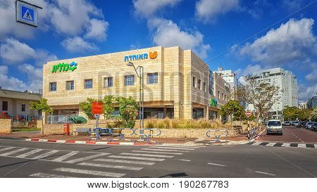 Rishon LeZion, Israel-April 14, 2016: Beautiful view of two-story yellow tiled building exterior with Hebrew letters flooded by sunset light under blue sky. There are two healthcare funds Meuhedet and Clalit. This service center is located at 8-10 Ha-Shir