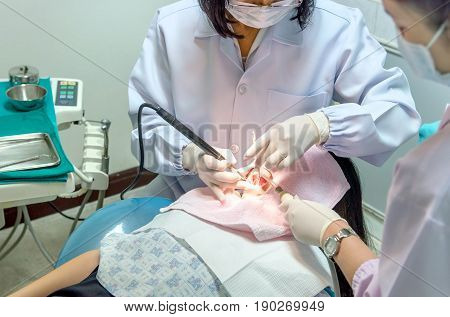 Close up fo Asian dentist examines young girl patient using mirror for teeth checkup and cleaning her teeth of tartar and plaque.