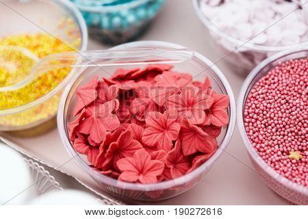 Ice cream treats and toppings sale. Rainbow sprinkles, non pareil and flower form glitter cupcake decorations, bright pink and red. Closeup in plastic plates with spoons. Confectionery store