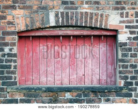 baorded up window in an old victorian building with faded wood and peeling red paint
