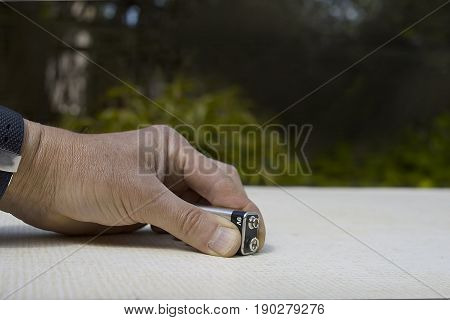 Male hand holding a 9 volt battery on a table top outdoor cropped shot