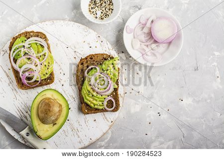 Sandwiches on toast grain dark bread with slices of avocado, sweet pink onions and multi-colored sesame seeds. Top view.