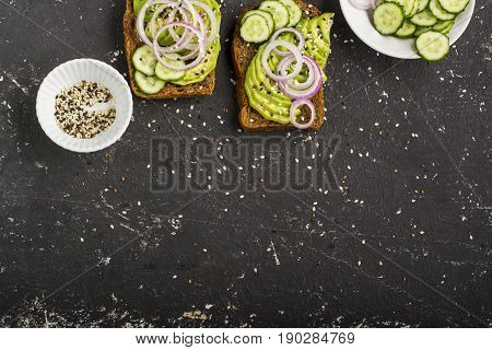 Sandwiches on toast grain dark bread with slices of avocado, sweet pink onions and multi-colored sesame seeds. Top view.