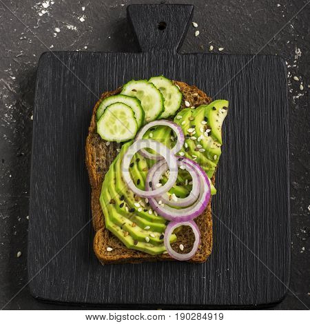 Sandwiches on toast grain dark bread with slices of avocado, sweet pink onions and multi-colored sesame seeds. Top view.