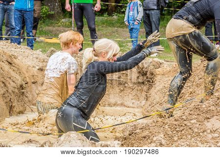 Stockholm Sweden - June 03 2017: Close up side view three caucasian woman struggling in a mud obstacle to complete the course of the annual event Toughest Stockholm. Water splash and people in the background.
