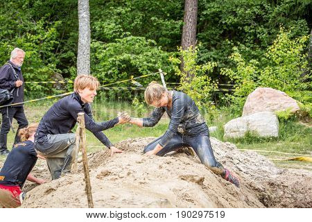 Stockholm Sweden - June 03 2017: Close up side view two caucasian athletes male and female struggling in a mud obstacle to complete the course of the annual event Toughest Stockholm. People in the background.