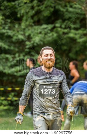 Stockholm Sweden - June 03 2017: Close up front view one caucasian man with full beard. Wet dirty and tired after completing a mud obstacle at the annual event Toughest Stockholm. A few people out of focus in the background.