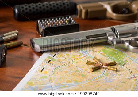 Close up of a shotgun and a revolver, cartridge belt with bullets on a map, on wooden table.