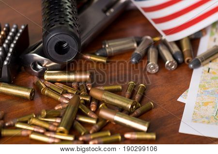 Close up of a shotgun and a revolver, cartridge belt with bullets with part of a blurred United States flag on a map, on wooden table.