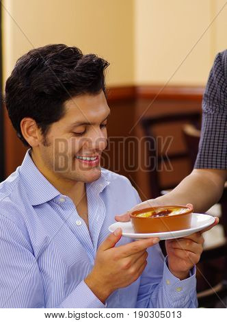 Handsome man is going to eat a turkish traditional dairy style rice pudding sutlac served in a crock on wood background.